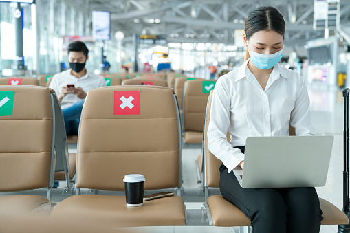 Social distancing, businesswoman sit working with laptop and smartphone keeping distance away from each other to avoid covid19 infection during pandemic. Empty chair seat red cross shows new normal