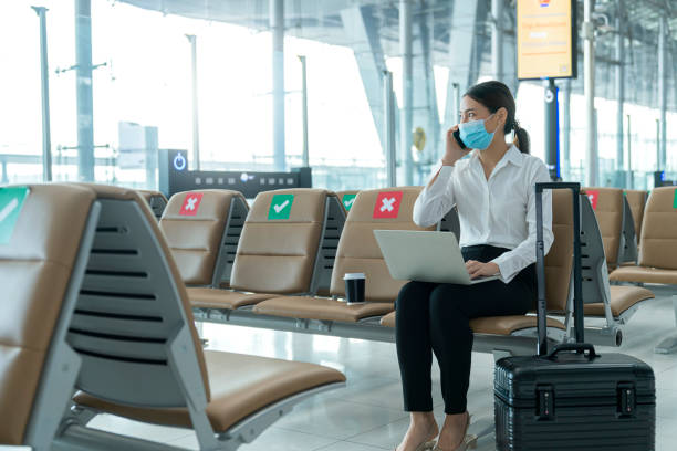 social distancing, businesswoman wearing face mask sit working with laptop keeping distance away from each other to avoid covid19 infection during pandemic. empty chair seat red cross shows new normal - business class imagens e fotografias de stock