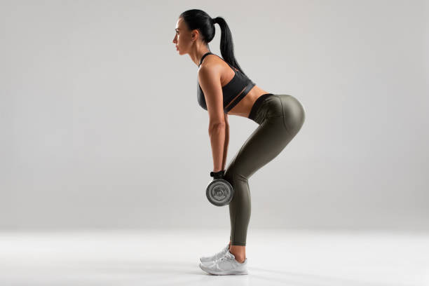 mujer de fitness haciendo ejercicio para glúteos sobre fondo gris. entrenamiento atlético chica con mancuernas - peso muerto fotografías e imágenes de stock