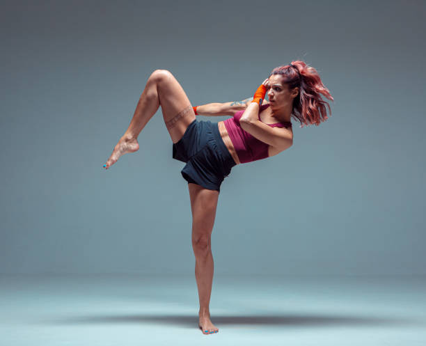 Athletic female fighter practicing kicks in studio isolated on gray background. Mixed martial arts poster Athletic female fighter practicing kicks in studio isolated on gray background. Mixed martial arts poster. High quality photo women boxing sport exercising stock pictures, royalty-free photos & images