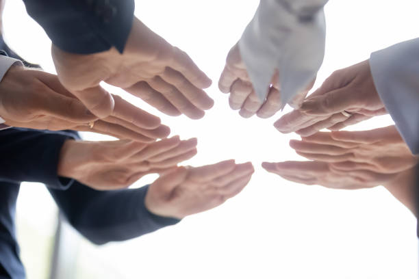 Teammates standing in circle spreading forward hands with palms down Group of diverse businesspeople teammates standing in circle together spreading forward hands with palms down like warming them by imaginary fire. Common goal, partnership, gender and age equality office buddies stock pictures, royalty-free photos & images