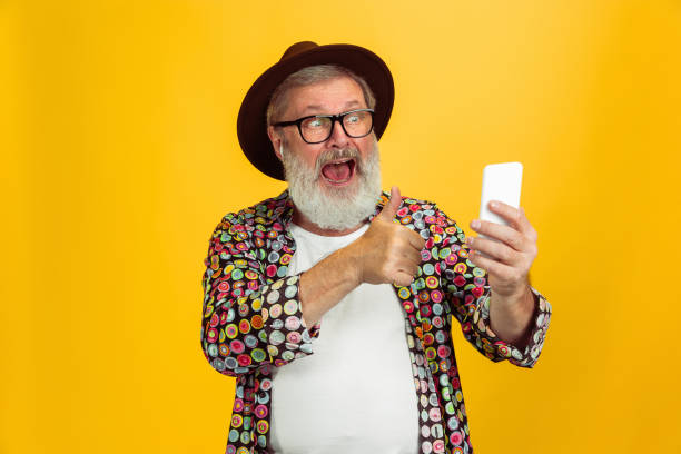 istock Senior hipster man wearing eyeglasses posing on yellow background. Tech and joyful elderly lifestyle concept 1268661737