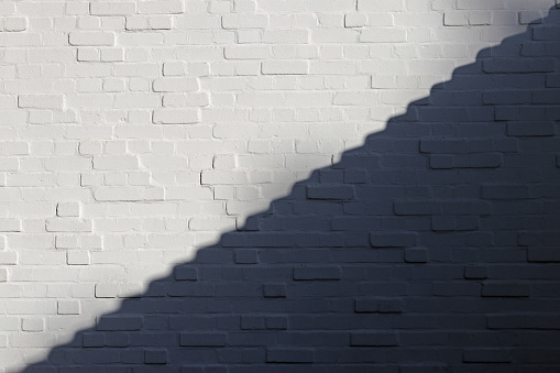 White brick wall is divided into light and shadow parts along the diagonal in form of steps. White and Black.