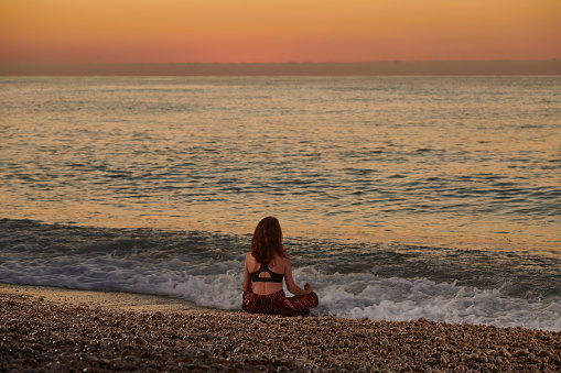 Yoga and meditation on calm beach at sunrise, Young fit women, Woman doing yoga outdoors at sunrise on the beach - Woman meditating at morning time - Fitness exercise concept for healthy lifestyle and positive mind - Main focus on the human silhouette