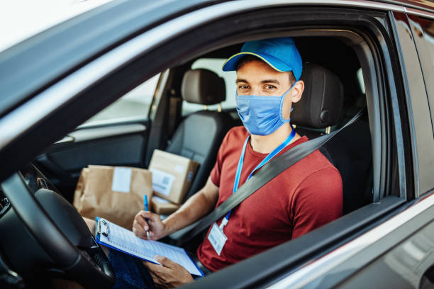 istock Smiling courier in the vehicle with face mask - delivery during quarantine 1268670158