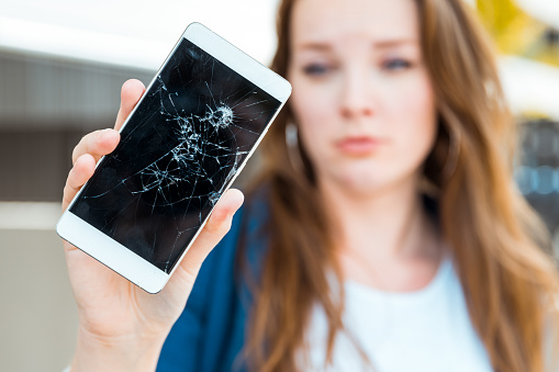 Young woman holding broken smartphone