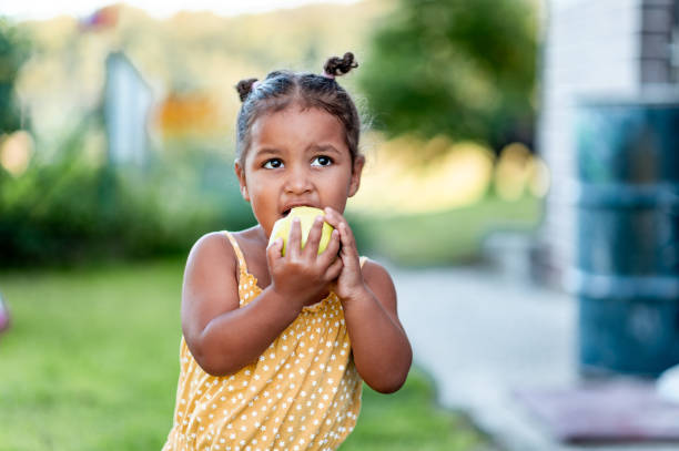 retrato de niña linda comiendo manzana al aire libre - apple healthy eating eating black fotografías e imágenes de stock