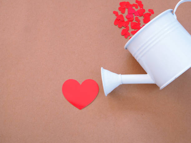 istock White watering plants and red hearts on brown paper background with copy space. 1268679818