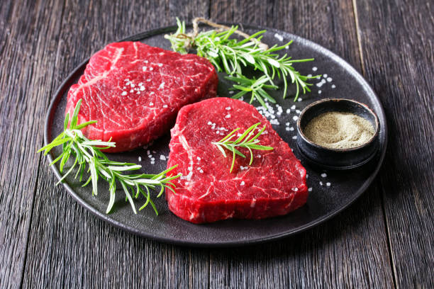 dry-aged beef steaks with rosemary and finely ground black peppercorn on a black stone plate uncooked beef steaks with rosemary and finely ground black peppercorn on a black stone plate, landscape view from above finely stock pictures, royalty-free photos & images