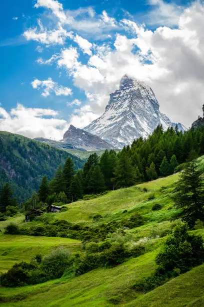 Vertical scenic view of the Matterhorn mountain summit with snow clouds blue sky and green nature during summer in Zermatt Switzerland