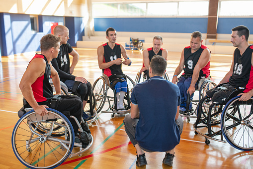 Rear view of coach meeting in gymnasium with male wheelchair basketball team and discussing strategy.