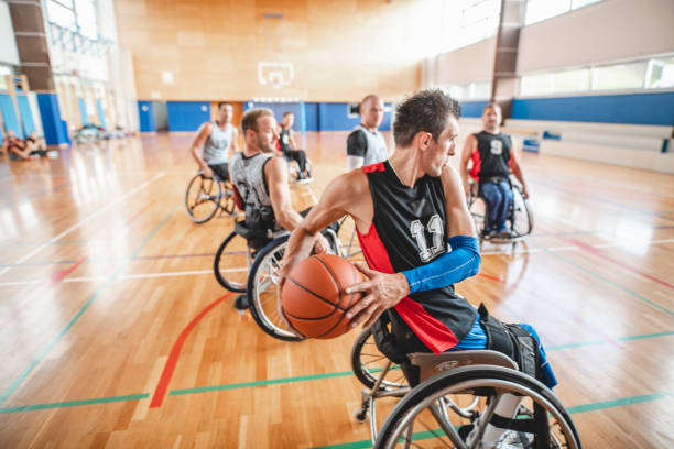 Close-up of male wheelchair basketball player in possession of ball and protecting it against opponents in practice game.