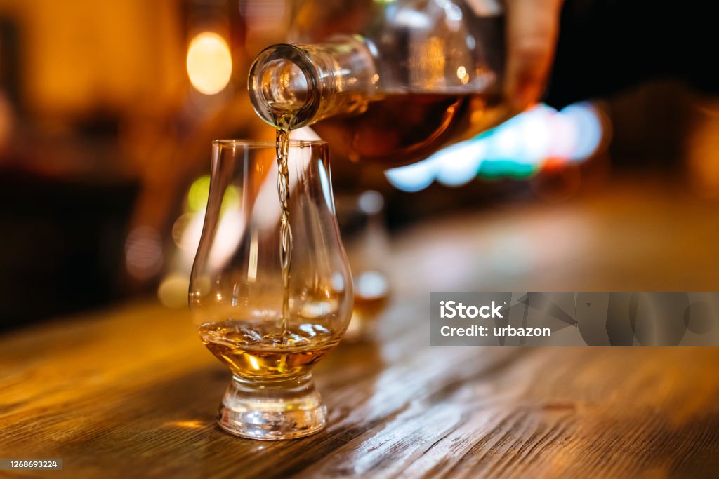 Pouring whiskey in glass Pouring whiskey in glass on bar counter. Whiskey Stock Photo