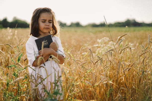 Girl holds bible in her hands. Reading the Holy Bible in a field. Concept for faith, spirituality and religion Girl holds bible in her hands. Reading the Holy Bible in a field. Concept for faith, spirituality and religion. Peace, hope Bible stock pictures, royalty-free photos & images