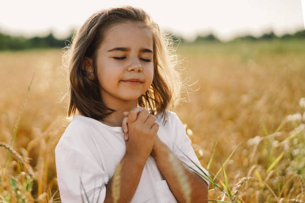 la petite fille ferma les yeux, priant dans un blé de champ. mains pliées dans la prière - fête religieuse photos et images de collection