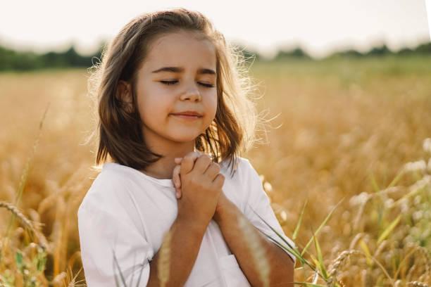 Little Girl closed her eyes, praying in a field wheat. Hands folded in prayer Little Girl closed her eyes, praying in a field wheat. Hands folded in prayer. Religion concept praying child religion god stock pictures, royalty-free photos & images