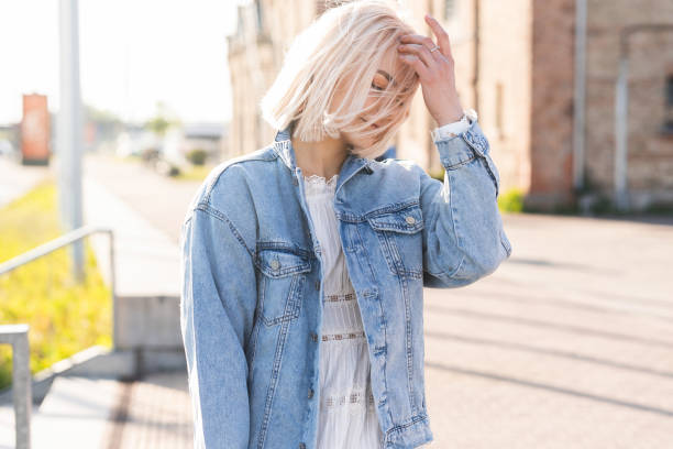 giovane ragazza bionda con i capelli a spettinato su una strada della città - denim jacket foto e immagini stock