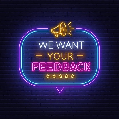 We want your feedback neon text in speech bubble frame with megaphone on brick wall background.