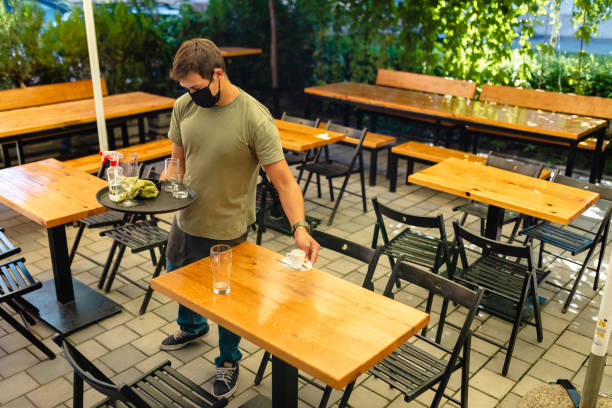 istock Handsome waiter holding a tray with a empty glasses while cleaning table after guests in his cafeteria 1268711824