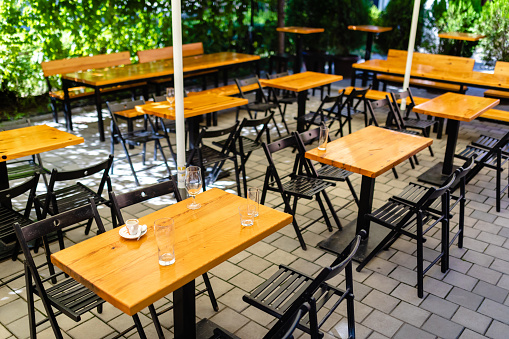 Empty outdoor coffee shop with tables and chairs. On a table there is a empty coffee cup, beer glass