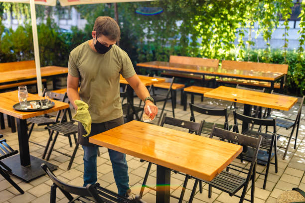 istock Waiter using spray bottle to apply a cleaning product so he can disinfect a table 1268711900
