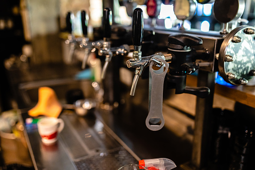 Beer dispenser and metal bottle opener on a bar counter at empty brewery