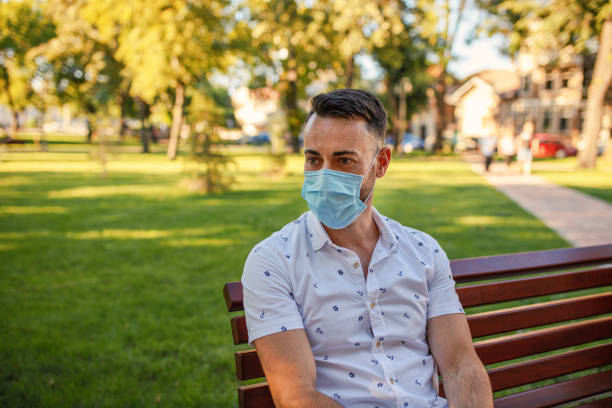 istock Young man in a protective mask, sitting on a bench in a city park 1268712160