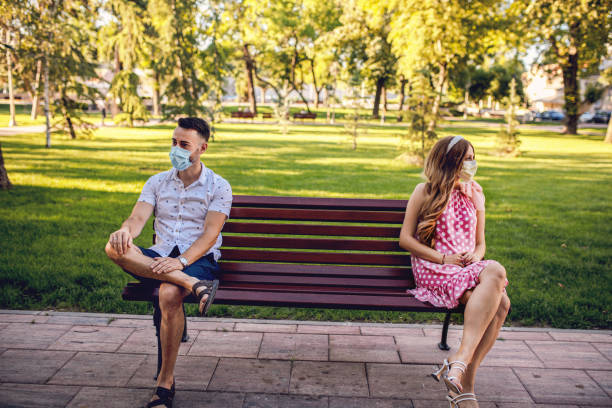 istock Man and woman with protective masks sitting on park bench while social distancing 1268712192