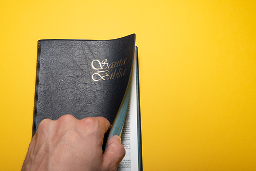 Man hand opening Santa Biblia (Holy Bible in spanish) on yellow