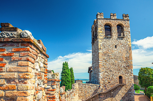 Stone tower with merlons on top and brick wall of old medieval castle Castello di Desenzano del Garda town, blue sky background, Lombardy, Northern Italy