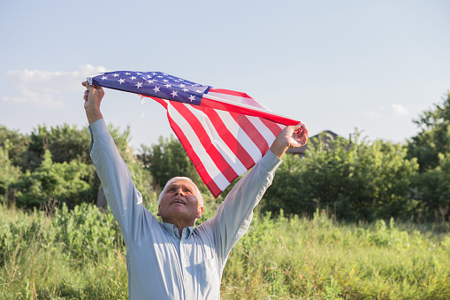 Patriotic senior man celebrates usa independence day on 4th of July with a national flag in his hands. Constitution and Citizenship Day. National Grandparents day