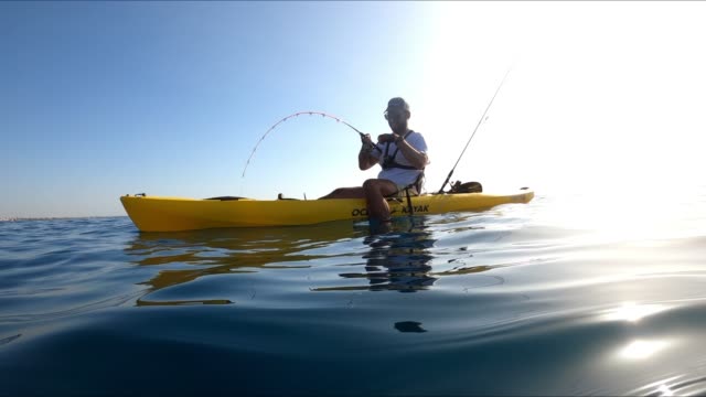 A sportsman fishing in kayak underwater view of fish hooked to a lure being pulled out of water.
