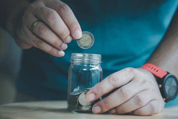 istock Man hand putting Thai coins in glass jar, idea saving money concept 1268719201