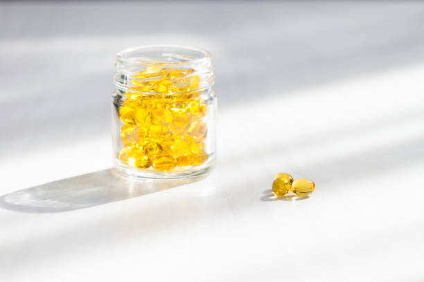 비타민 d를 곁들인 옐로우 캡슐, 흰 나무 배경에 햇빛이 있는 생선 기름 오메가 3. 건강하고 의료적 개념. - vitamin d capsule fish oil yellow 뉴스 사진 이미지