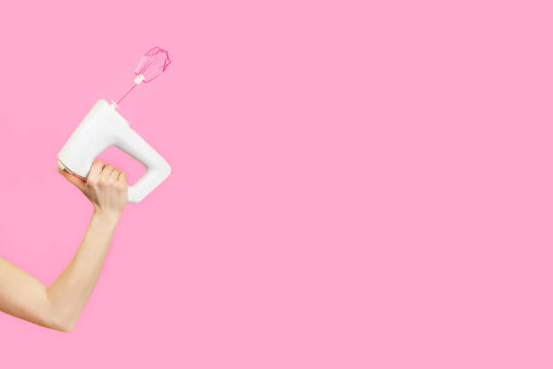istock White kitchen mixer in female hand isolated on pink background. 1268721143
