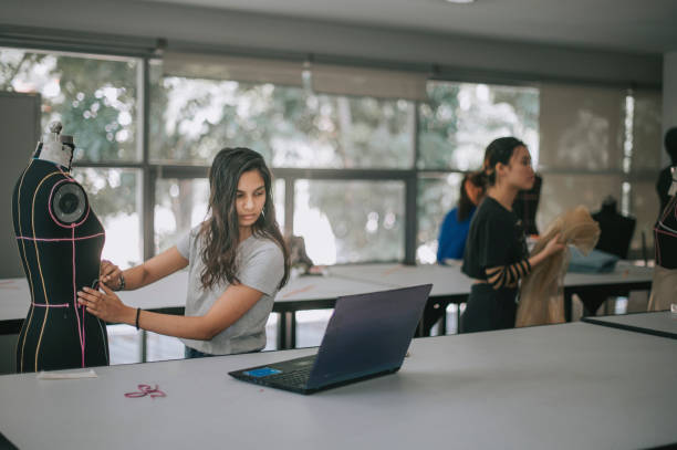 college fashion student attending class in the classroom working on their fashion design project with mannequin college fashion student attending class in the classroom working on their fashion design clothing design studio stock pictures, royalty-free photos & images