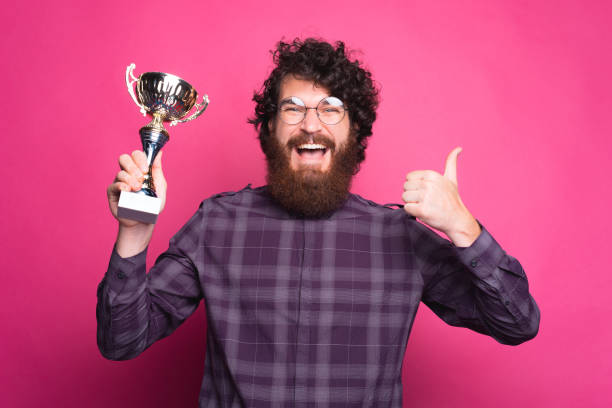 istock Joyful bearded man is holding a winner cup and thumb up 1268724611