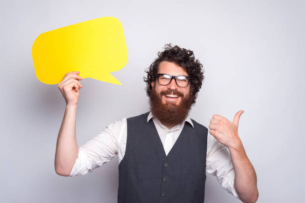 photo of cheerful young hipster guy holding epmty yellow speech bubble - epmty imagens e fotografias de stock