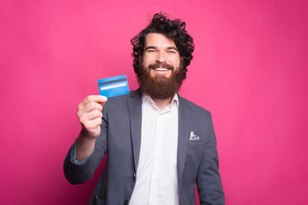 istock Happy bearded man in suit showing blue credit card 1268724905