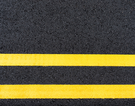 Freshly painted double yellow road marking lines, on newly laid asphalt.