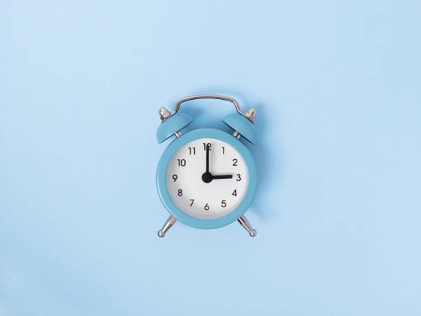 istock Retro alarm clock middle of blue background. Monochrome simple flat lay with pastel texture. Time concept. Stock photo. 1268741137