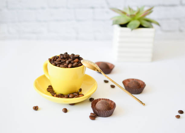 istock A yellow cup with natural coffee beans, on a white background, and chocolates. Concept of morning coffee. Flowers in the background. 1268780923