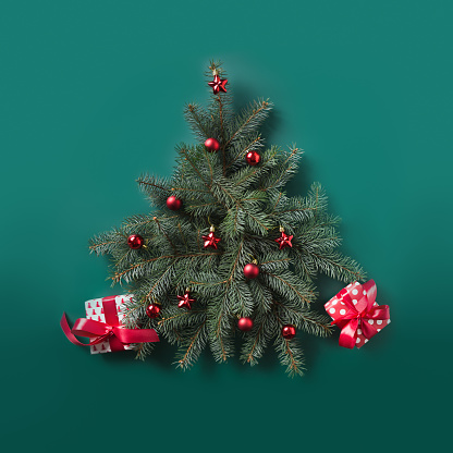 Christmas tree made of fir branches and red balls decorated red gifts on green. Flat lay. Top view. Xmas square greeting card.
