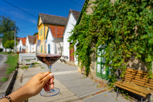 Glass of red wine with many colorful old traditional wine cellers in Villanykovesd in a hungarian wine region called Villany .