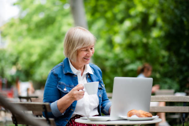 istock Senior woman with coffee sitting outdoors in cafe, using laptop. 1268803979