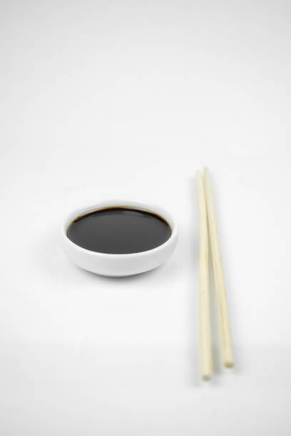 soy sauce in a small white bowl and bamboo chopsticks, isolated on white