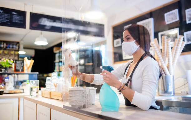 Young woman with face mask working indoors in cafe, disinfecting counter. Portrait of young woman with face mask working indoors in cafe, disinfecting counter. STORE CLEANLINESS stock pictures, royalty-free photos & images