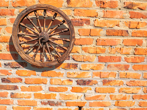 Old wooden wheel on a brick wall. Wooden wheel of a horse carriage. Red brick wall. Decor element. Retro style. Background image. Place for your text.