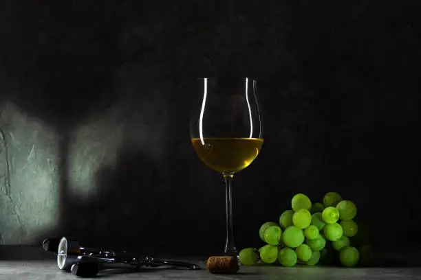 Photo of White grapes and a glass of white wine with a shadow in the background.