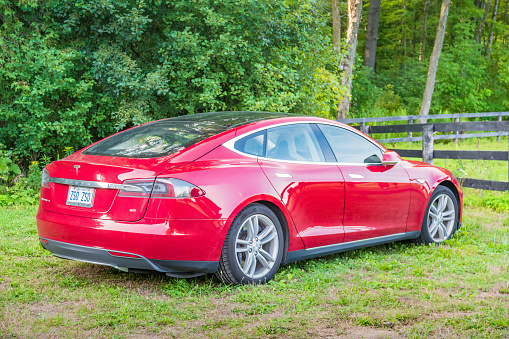 A red colored Tesla Model S is parked on a lawn near Kitchener, Ontario on a summer evening.